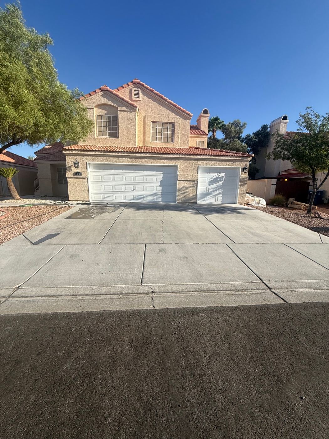 Dusty, stained concrete driveway in front of a tile-roof home with a closed three-car garage