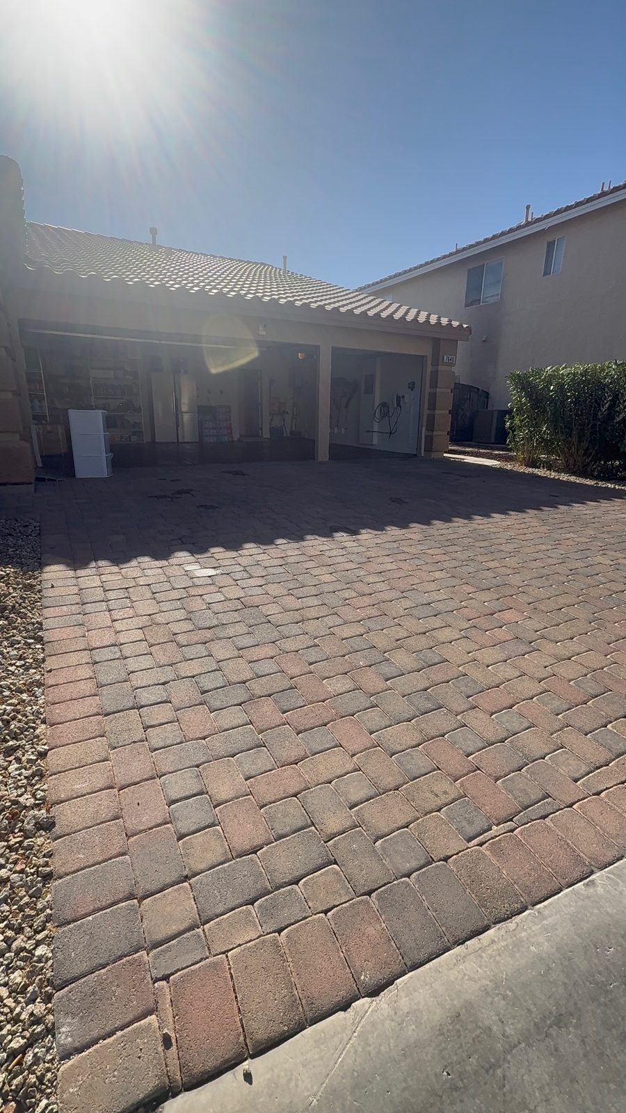 Dull, dusty multicolor paver driveway in shadow near an open garage, with sun glare overhead